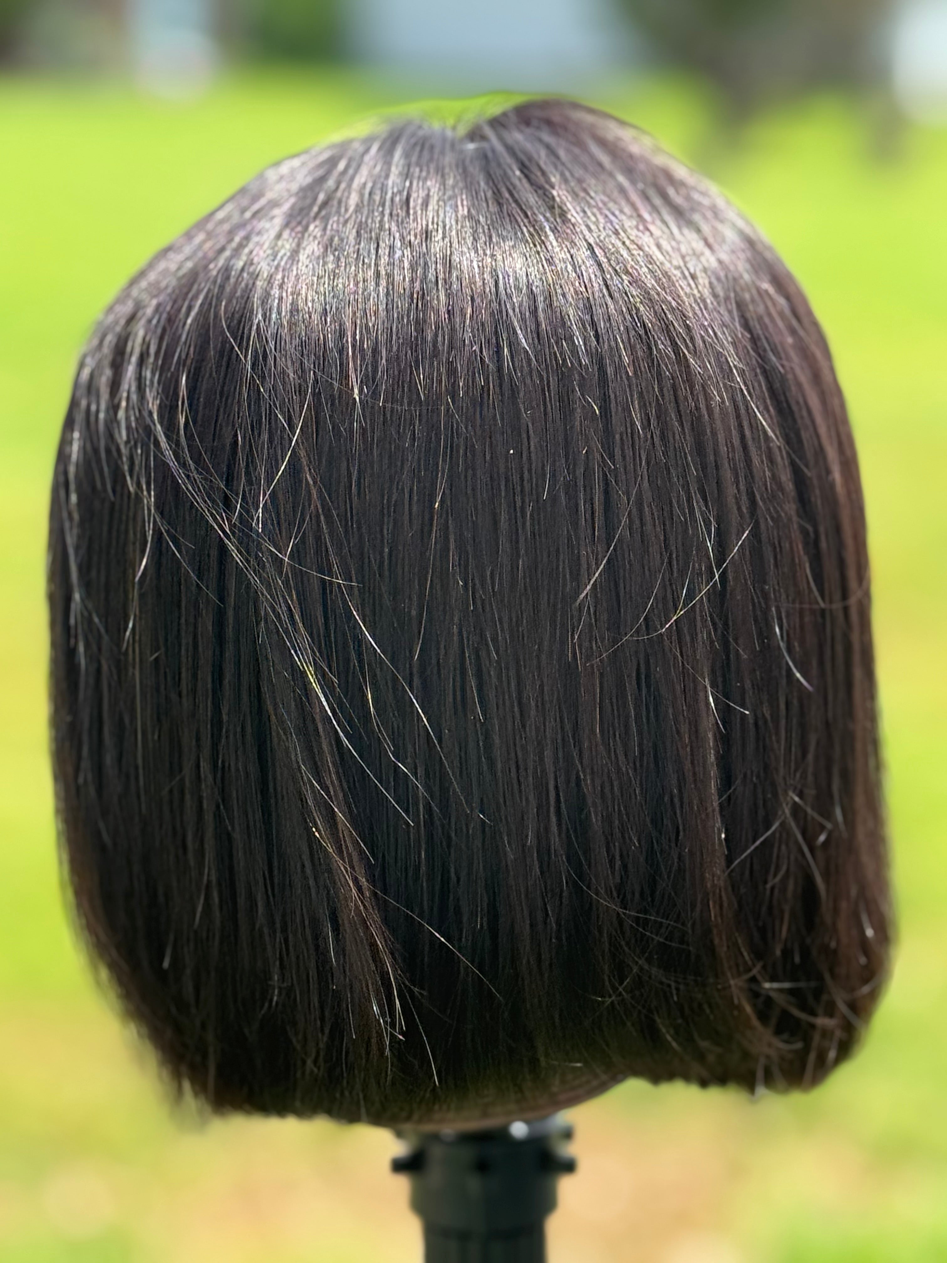 Black bob wig on a mannequin head with a blurred green outdoor background