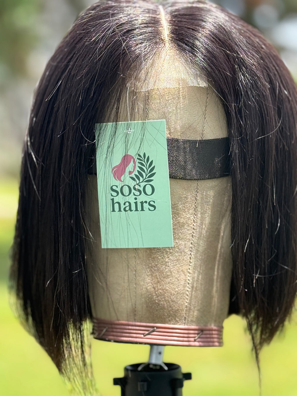 Mannequin head with a wig and a 'Soso Hairs' label against a blurred outdoor background